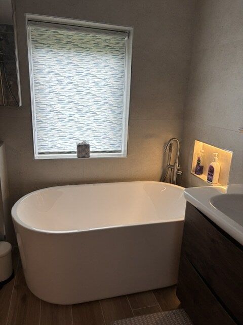 Freestanding bath beside a dark vanity unit and illuminated bathroom storage niche.