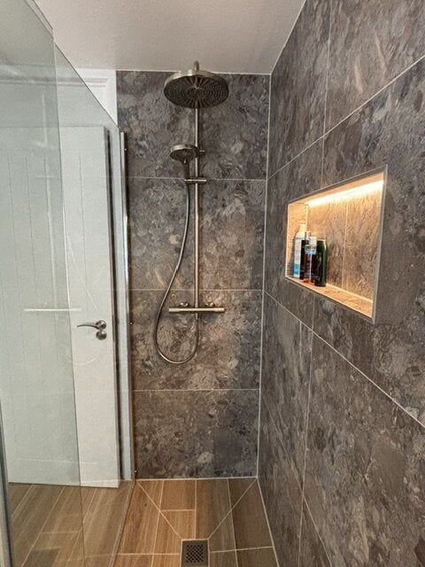 Walk-in shower with dark stone-effect tiles, rainfall shower and illuminated recessed shelf.