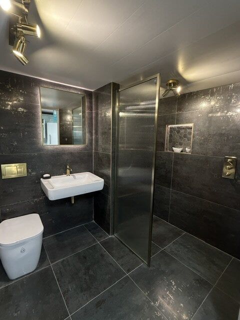 Dark luxury bathroom display at Easy Bathrooms High Wycombe featuring charcoal tiles, white basin and brushed brass details.