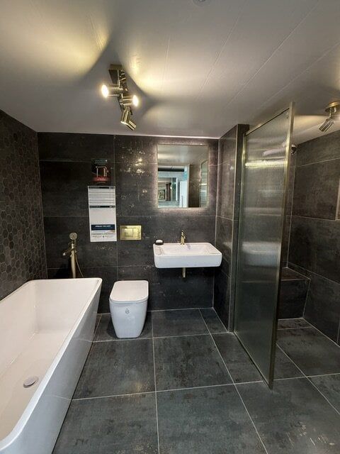 High Wycombe bathroom display with freestanding bath, dark tiles, white sanitaryware and brushed brass fittings.