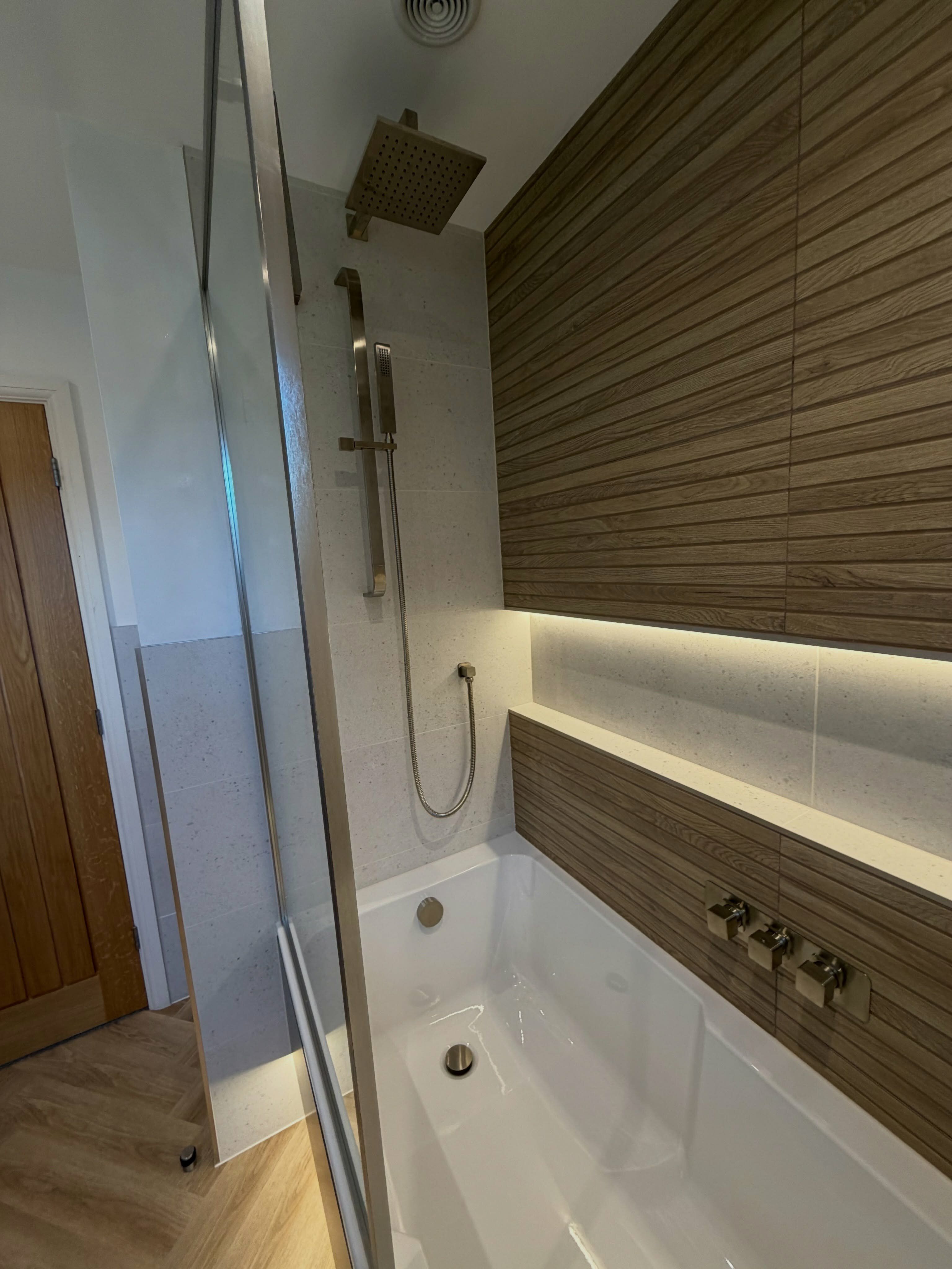 Close-up of the renovated shower area with wood-effect wall tiles and integrated shelf lighting.