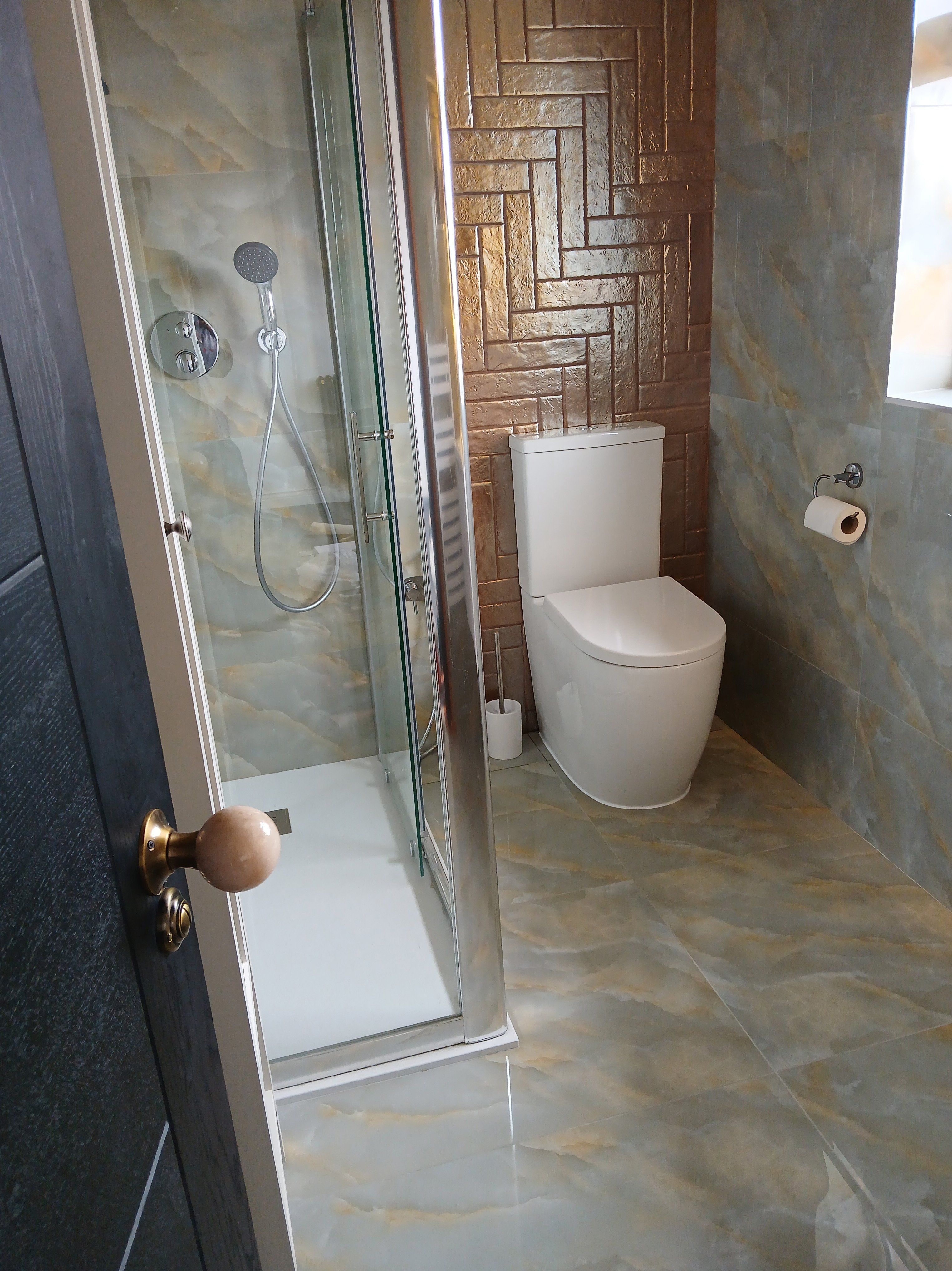 Small bathroom featuring a glass shower enclosure, white toilet and glossy marble-effect wall and floor tiles.