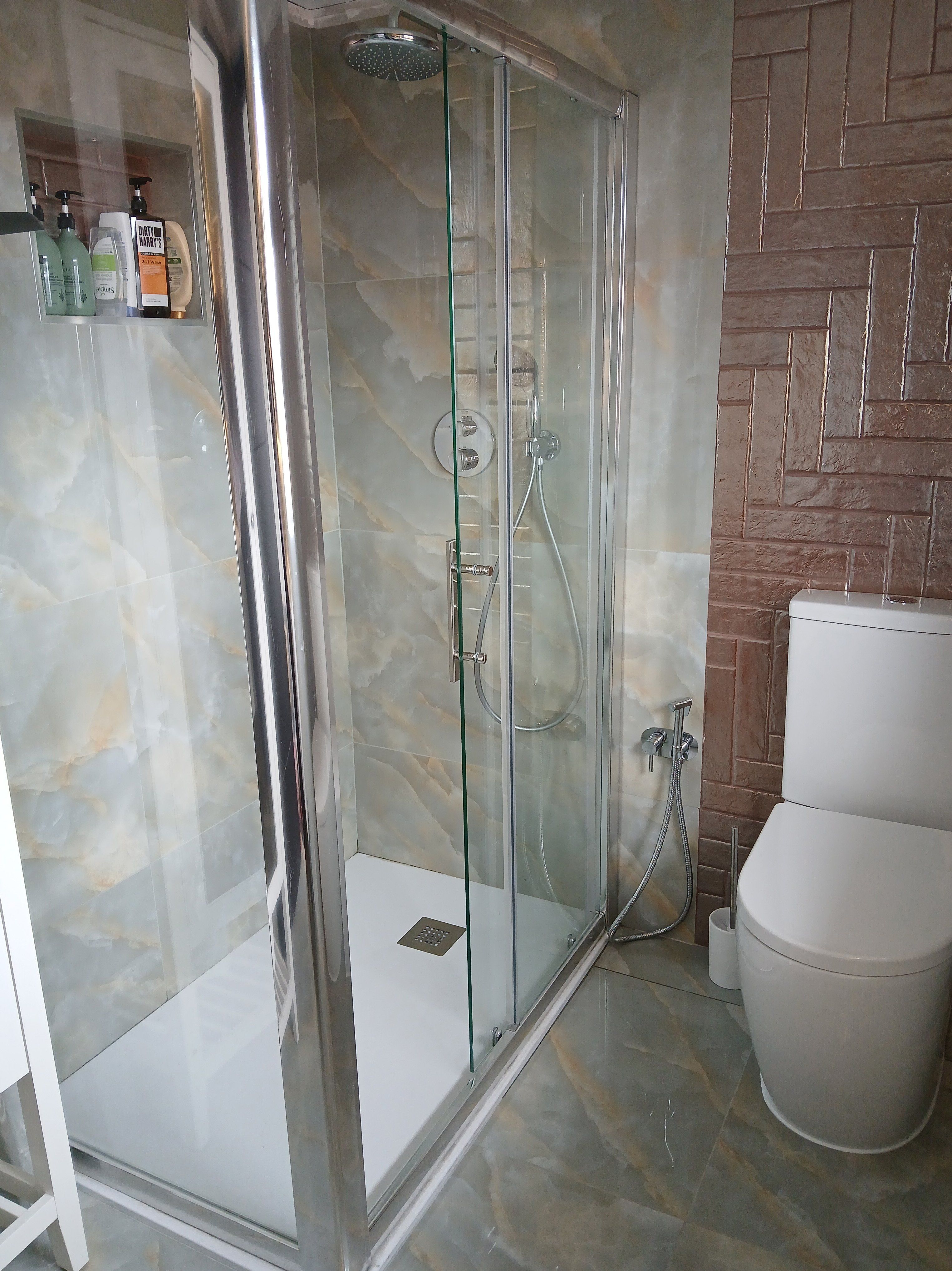 Compact bathroom with a glass shower enclosure, white toilet and contrasting bronze herringbone wall tiles.