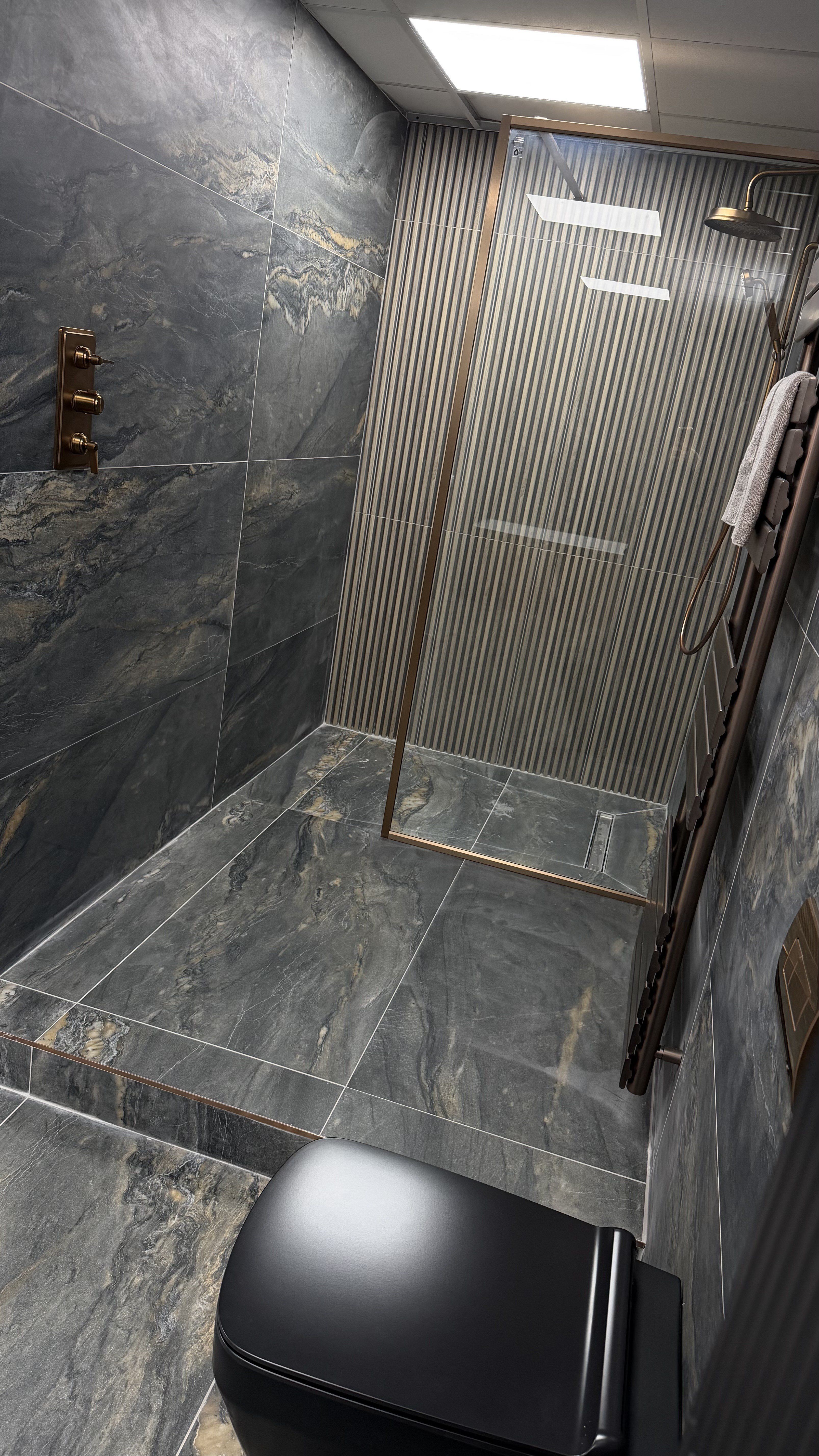 Modern bathroom display with a walk-in shower, dark stone-effect tiles and black toilet at the Easy Bathrooms High Wycombe showroom.