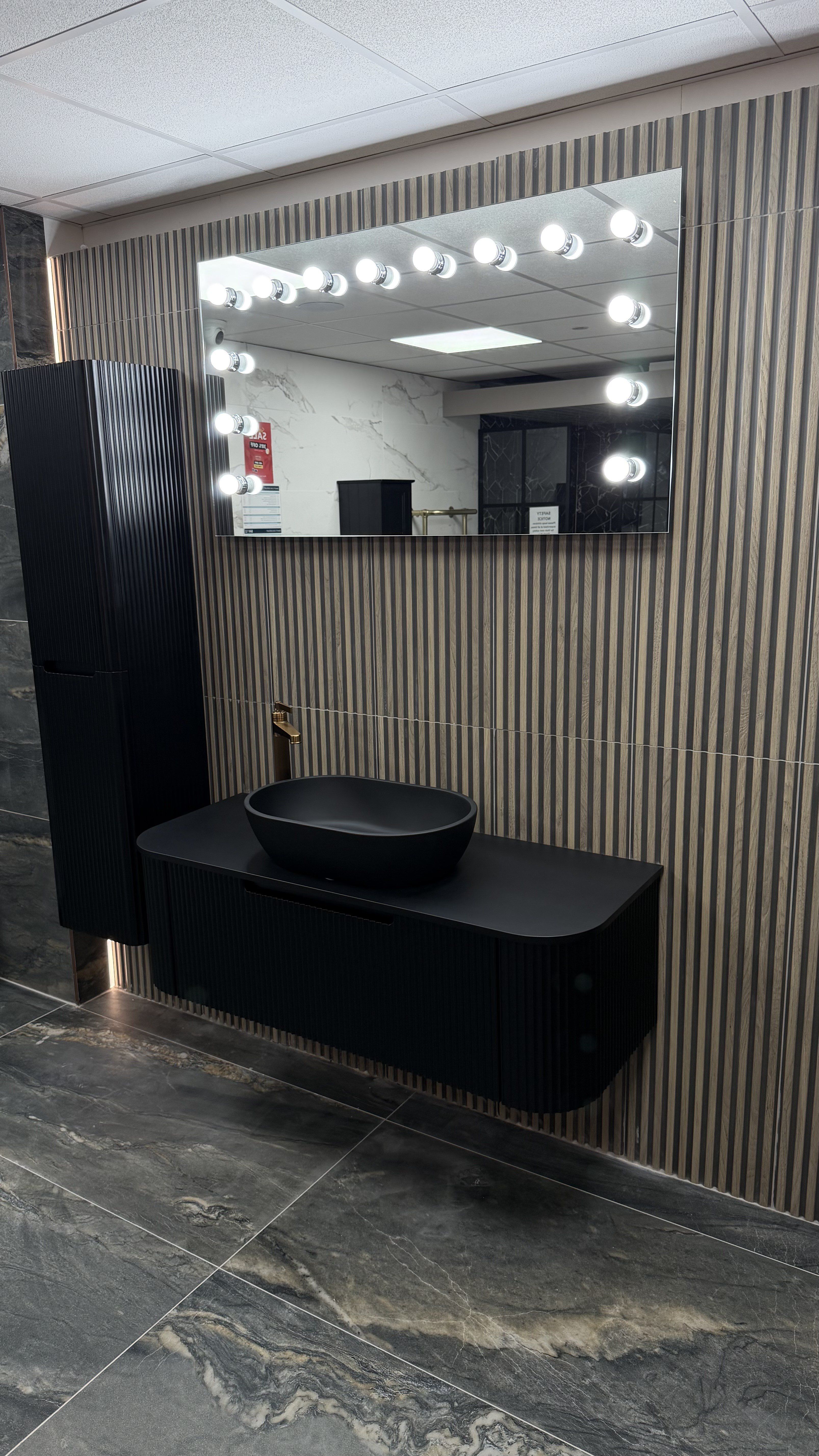Contemporary black wall-hung vanity unit with illuminated mirror and vertical feature tiles at the Easy Bathrooms High Wycombe showroom.