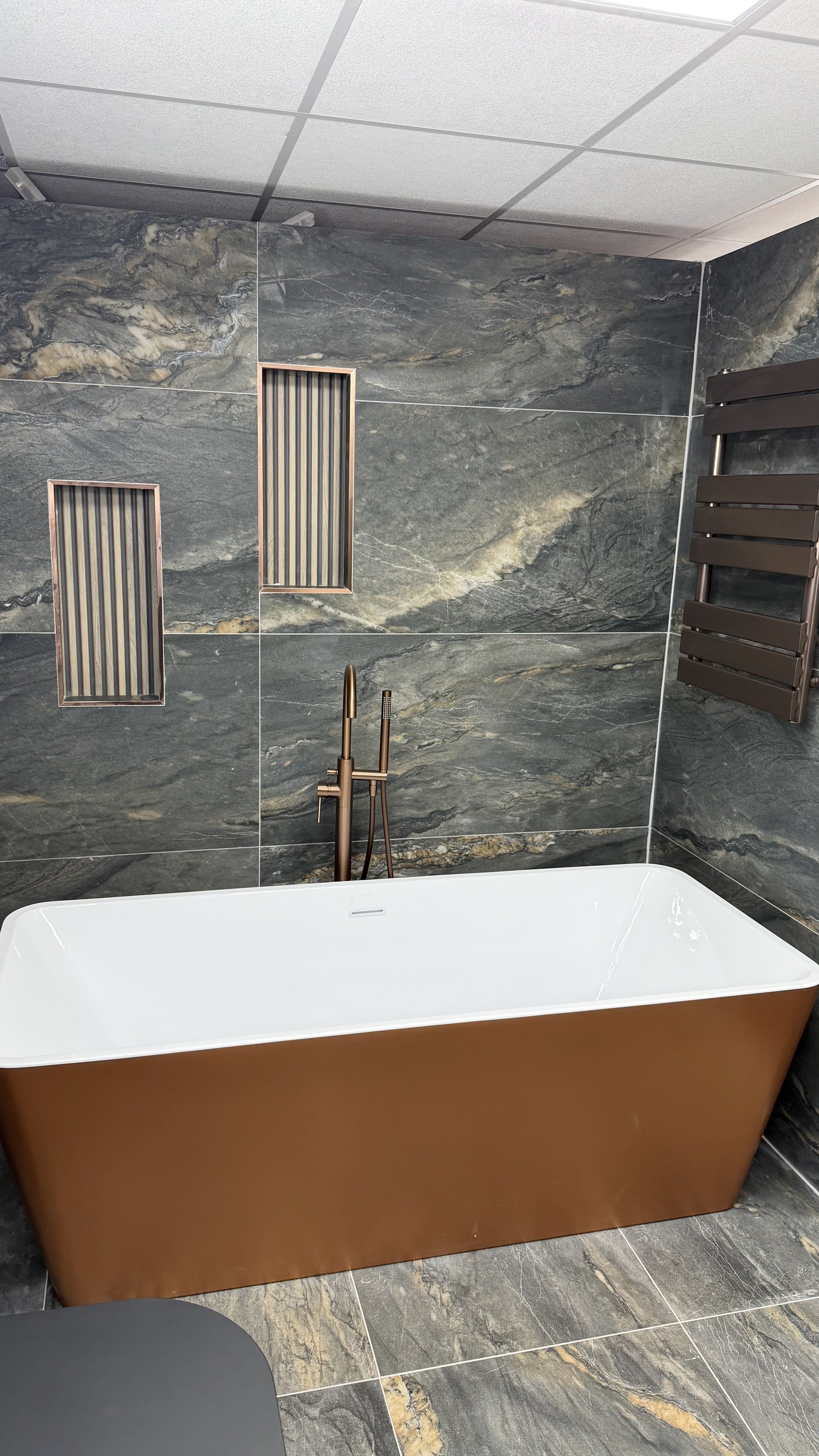 Freestanding bath with brushed bronze fittings and dramatic stone-effect wall tiles at the High Wycombe bathroom showroom.