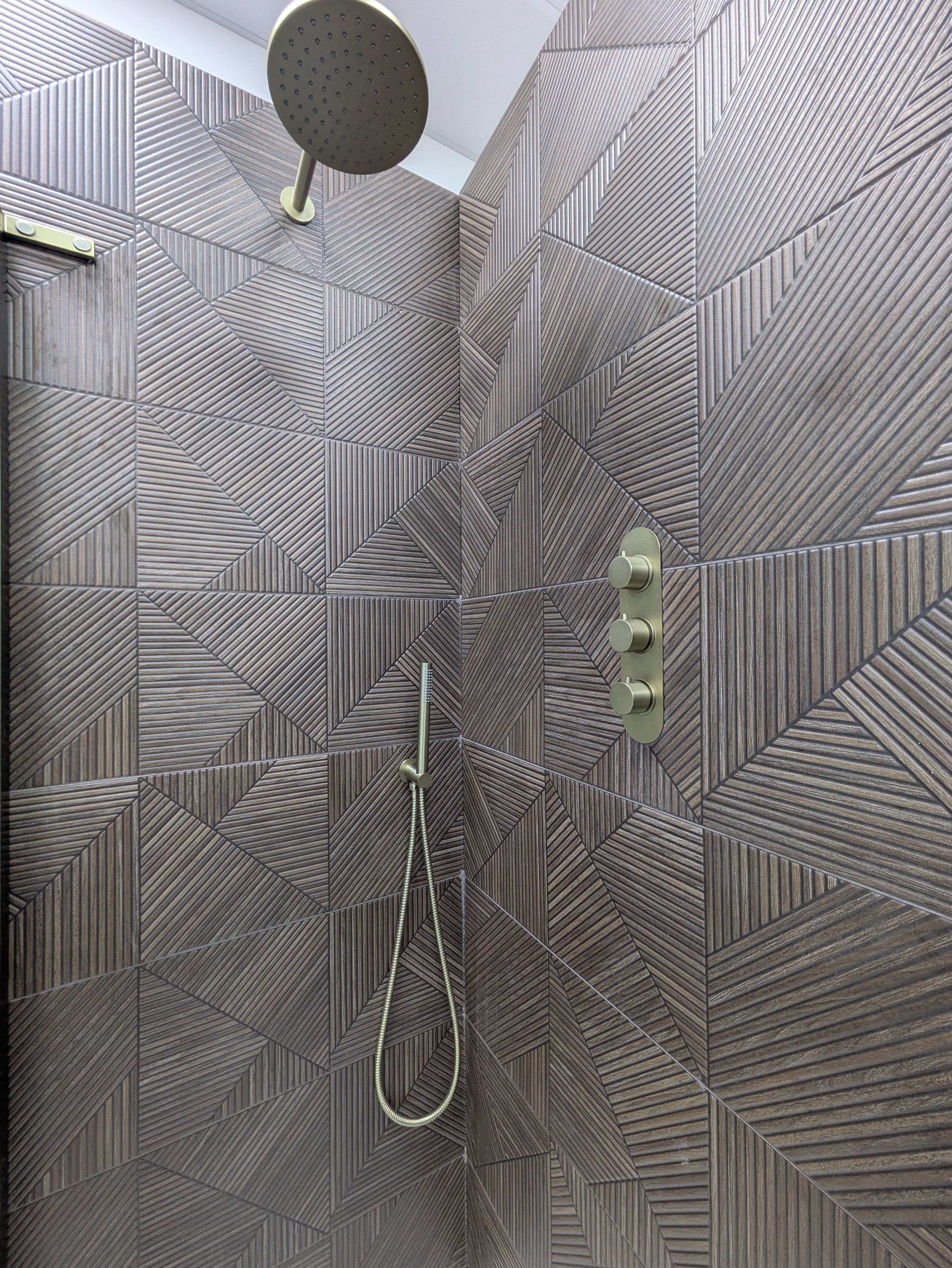 Walk-in shower with brushed gold fittings and dark textured wood-effect wall tiles.