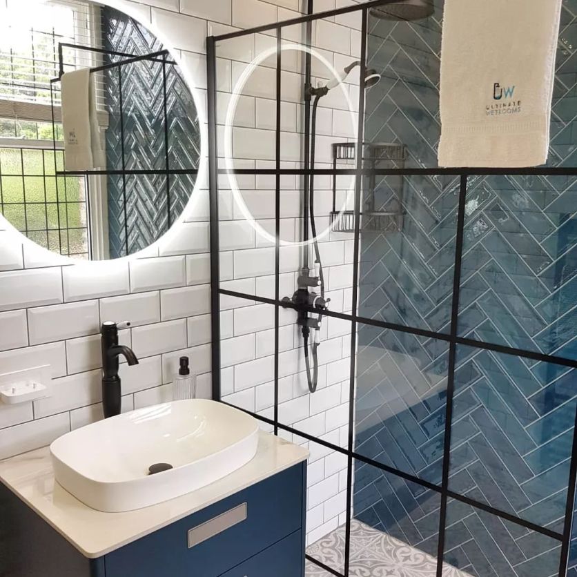Modern bathroom with blue herringbone shower tiles, black grid shower screen, white metro tiles and a petrol-blue vanity unit.