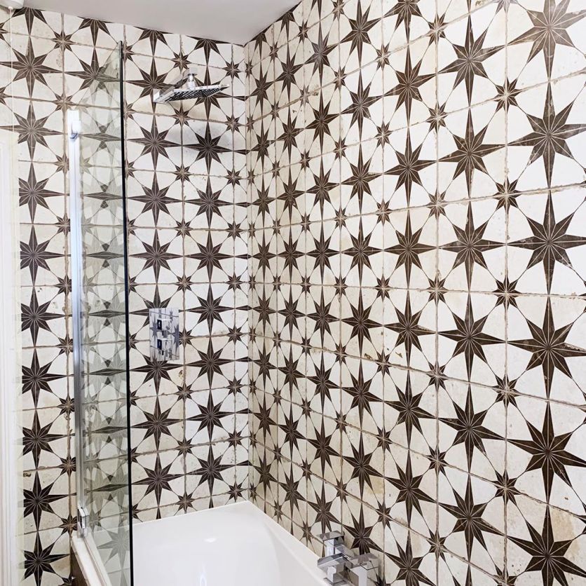 A striking shower wall featuring vintage-inspired star patterned tiles in a monochrome palette, complemented by a modern chrome rainfall shower head and a sleek glass screen.