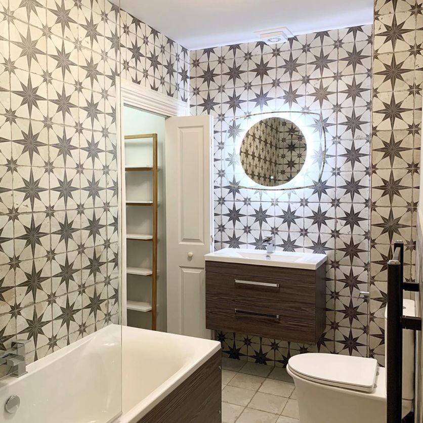 A stylish bathroom featuring a bold monochrome star-patterned tile feature wall, a dark wood-effect wall-hung vanity unit with a white basin, and a contemporary circular LED illuminated mirror.