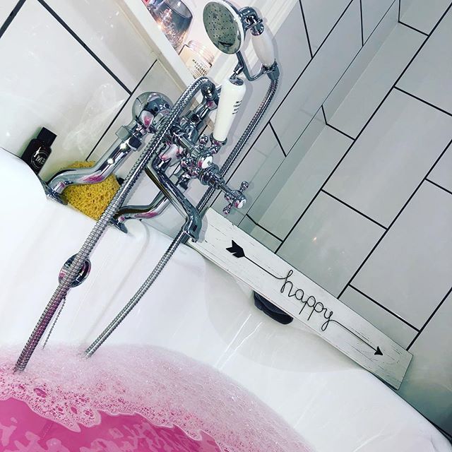 A close-up of a traditional chrome telephone-style bath shower mixer tap with white ceramic lever handles, mounted on a white roll-top bath against a backdrop of white metro tiles with contrasting dark grout.