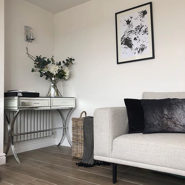 A modern white horizontal designer radiator with a slim column profile, elegantly positioned behind a mirrored console table on grey wood-effect flooring.