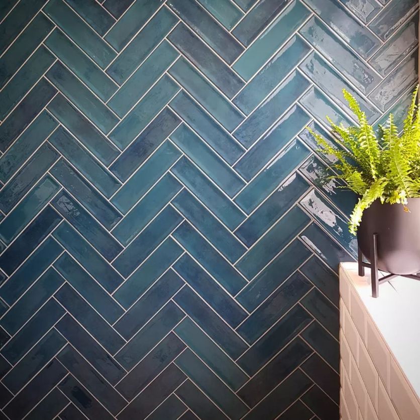 Stunning peacock blue gloss metro tiles arranged in a sophisticated herringbone pattern, creating a vibrant and textured feature wall in a modern bathroom.