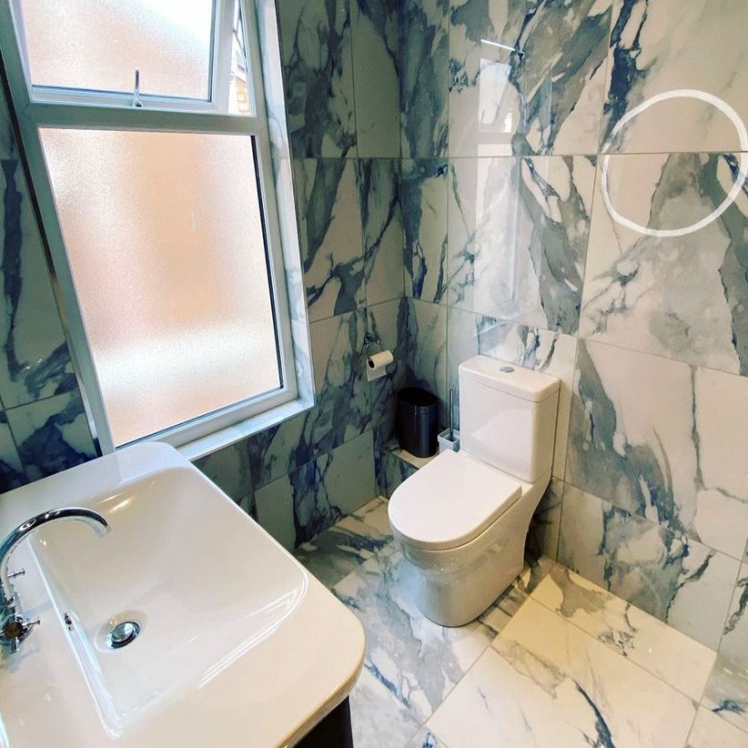 A modern cloakroom featuring dramatic blue and white marble-effect porcelain wall and floor tiles, paired with a sleek white back-to-wall toilet and a contemporary rectangular washbasin with a polished chrome mixer tap.