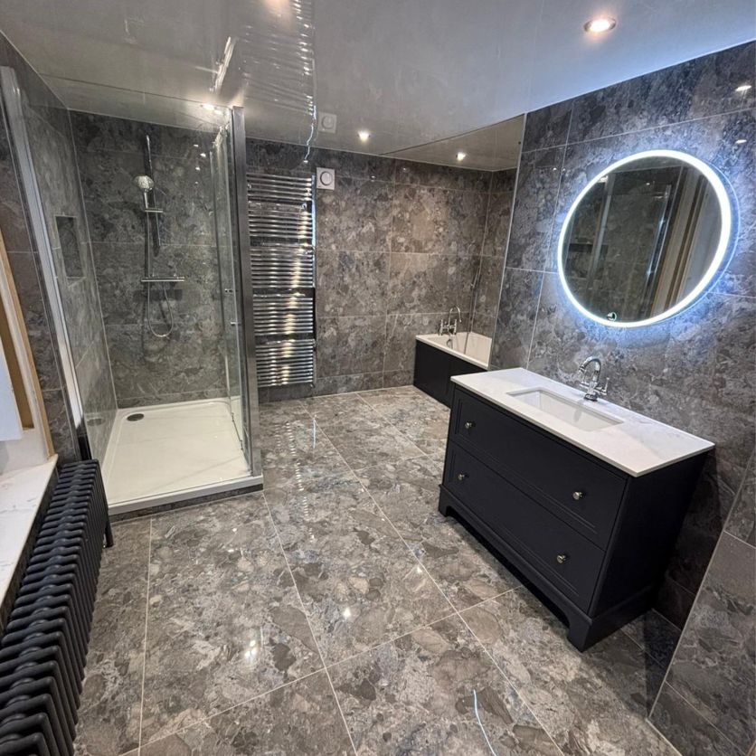A spacious luxury bathroom featuring Stevenage Blue Gloss marble-effect porcelain wall and floor tiles, paired with a navy traditional vanity unit and a Zia round LED illuminated mirror.