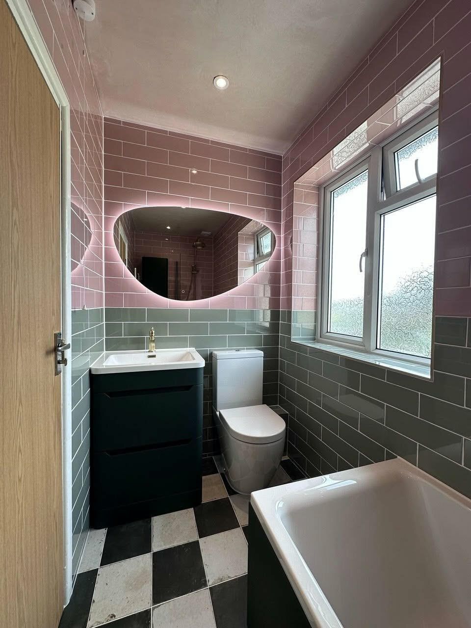 Completed colourful bathroom with forest green furniture, pink and green wall tiles, black-and-white flooring and brushed gold fittings.