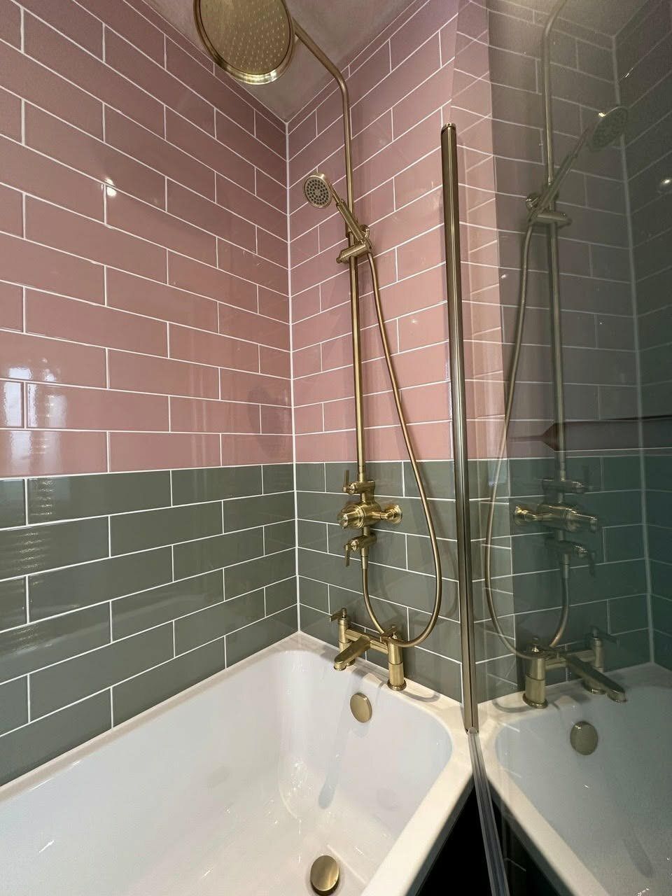 White bath with brushed gold shower fittings and bath screen against pink and green gloss wall tiles.
