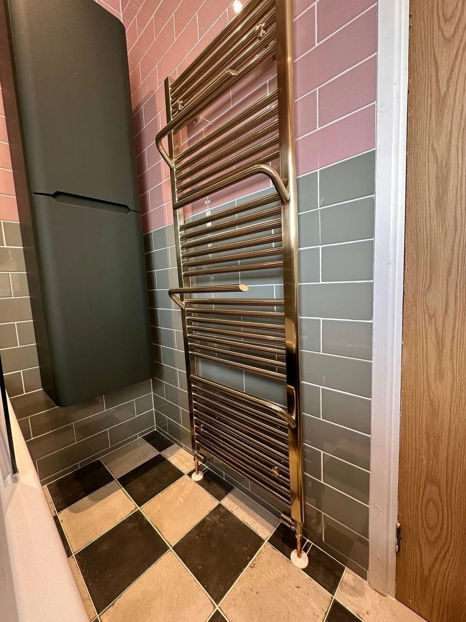 Brushed gold towel warmer beside a forest green storage unit and black-and-white tiled floor.