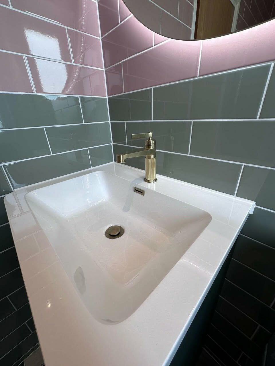 Brushed gold towel warmer beside a forest green storage unit and black-and-white tiled floor.