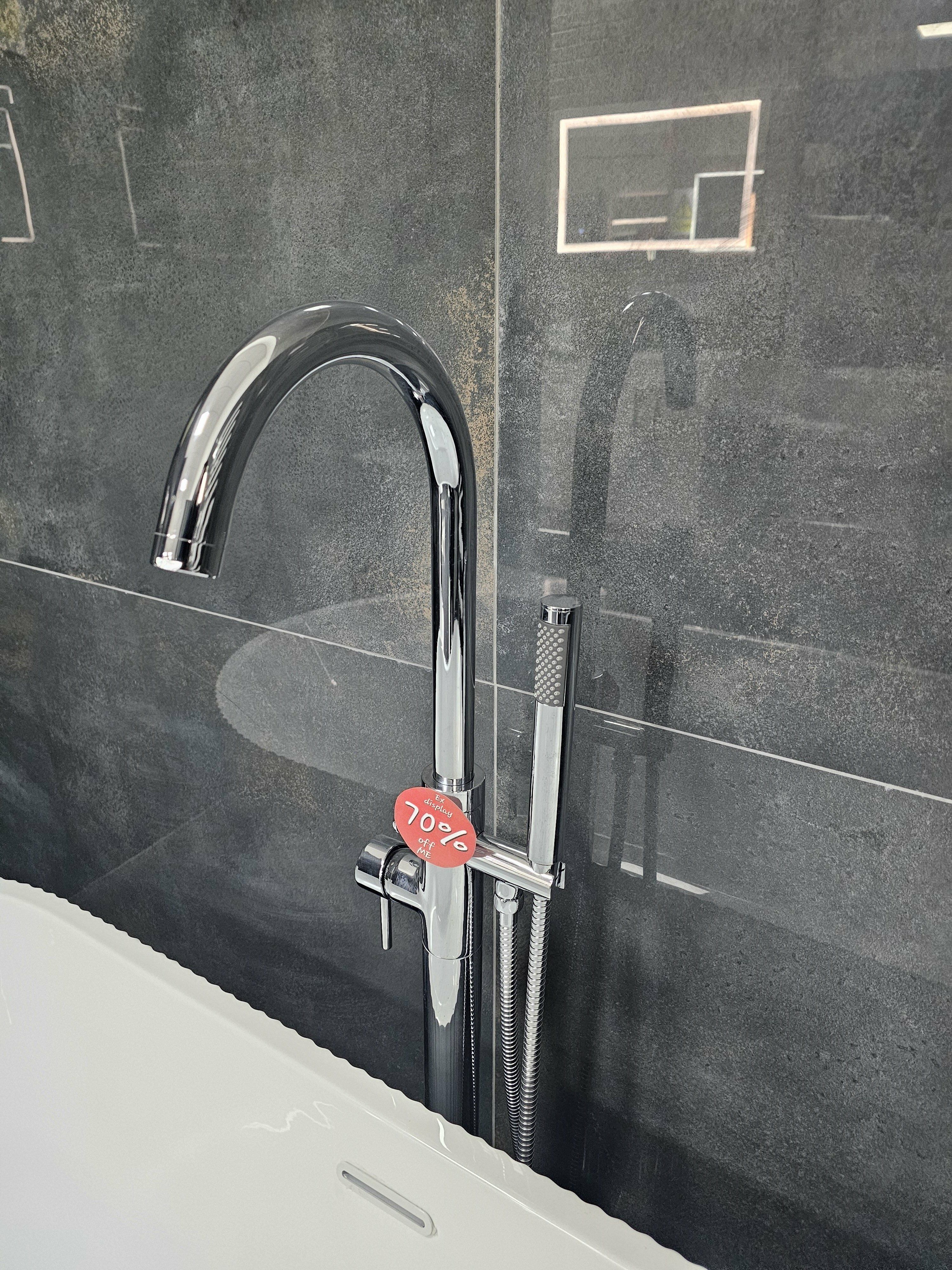 Chrome ex-display bath filler tap fitted beside a white bath against dark grey tiles.