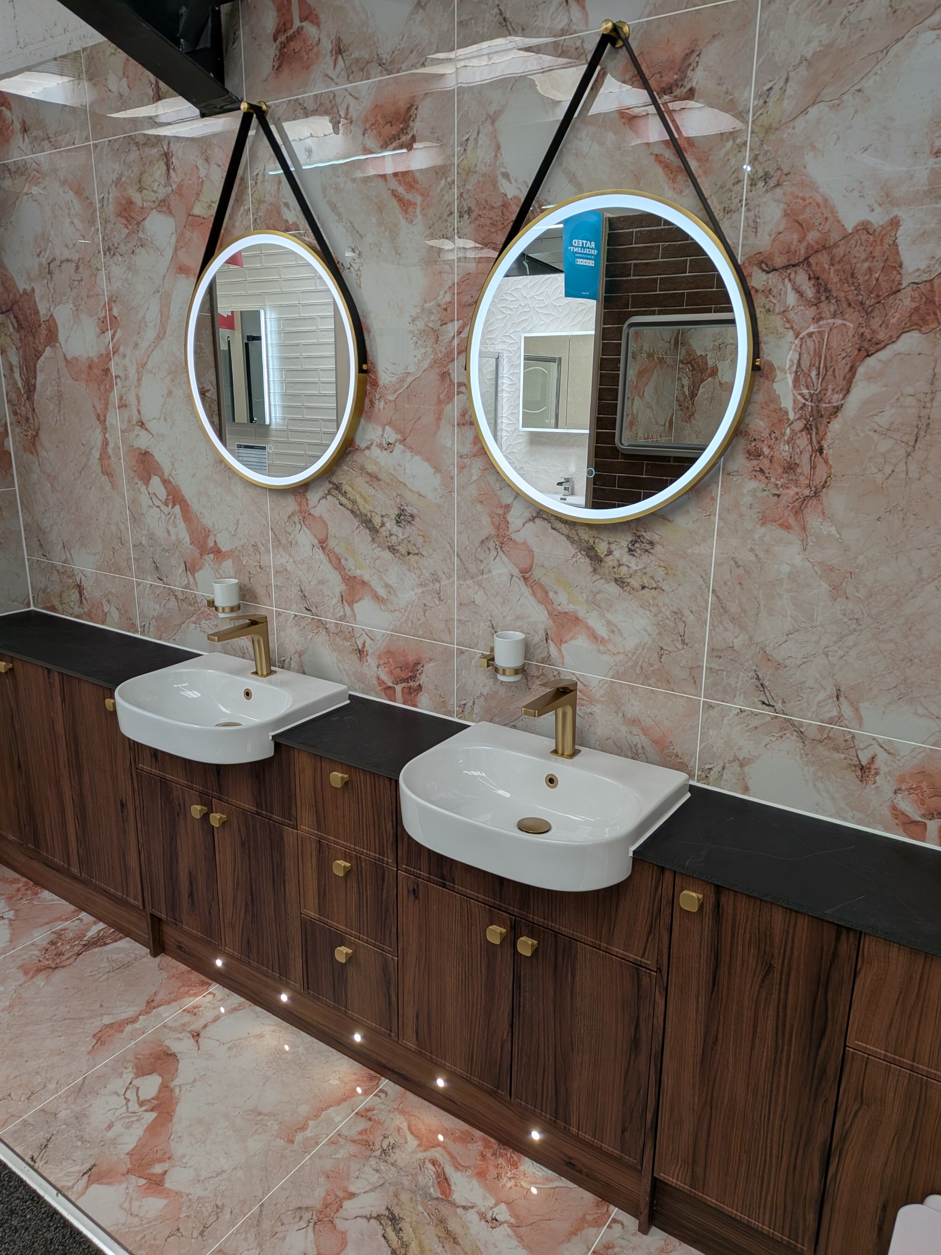 Rayleigh bathroom display with dark walnut furniture, marble-effect tiles, illuminated mirrors and brushed gold basin taps.