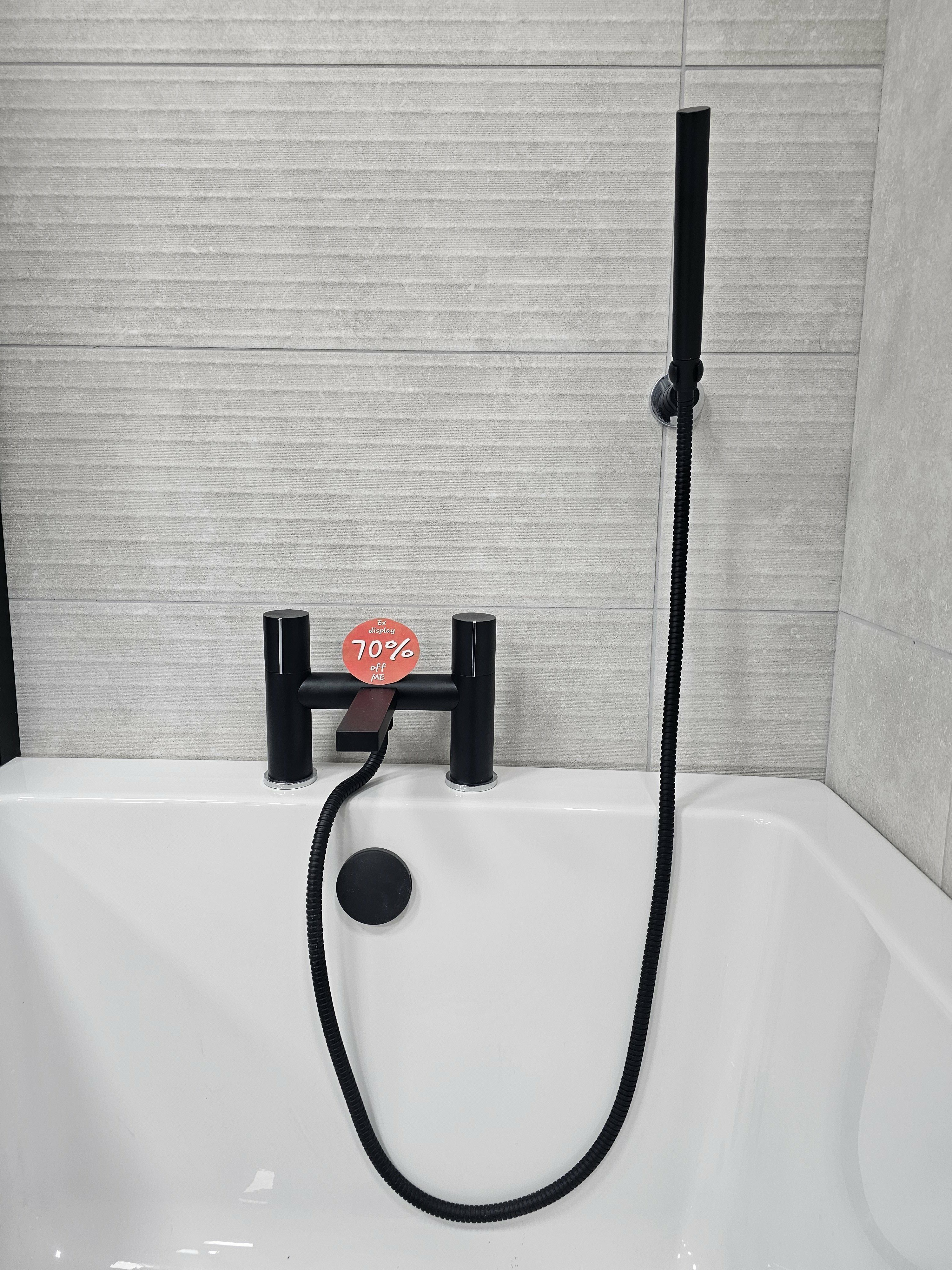 Black ex-display bath shower mixer and handset fitted above a white bath at the Folkestone showroom.