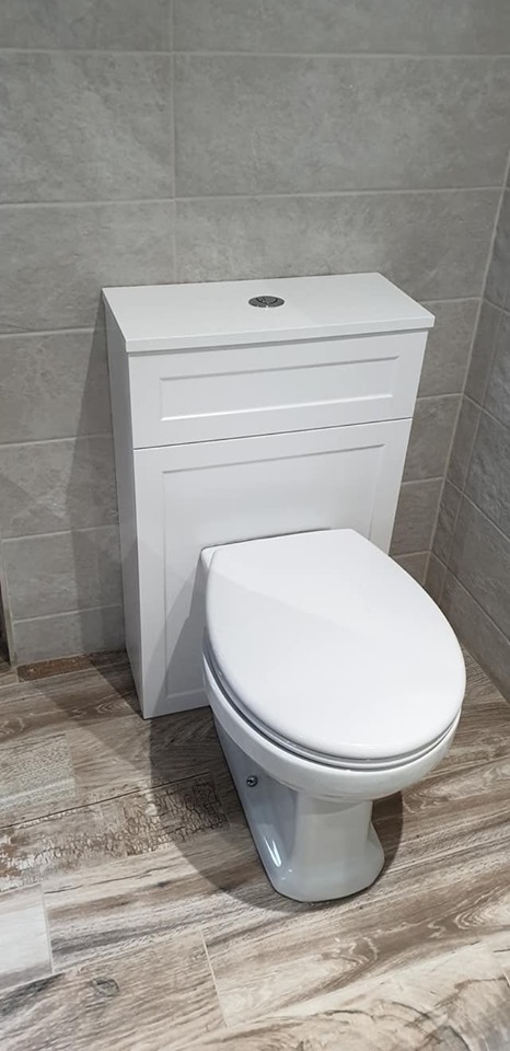 A white shaker-style back-to-wall toilet unit with a concealed cistern, positioned against textured grey wall tiles and complemented by rustic wood-effect floor tiling.