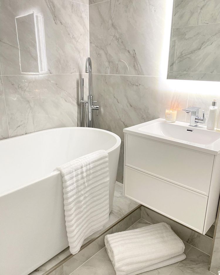 Modern white marble bathroom with freestanding bath, wall-hung vanity and soft ambient lighting.