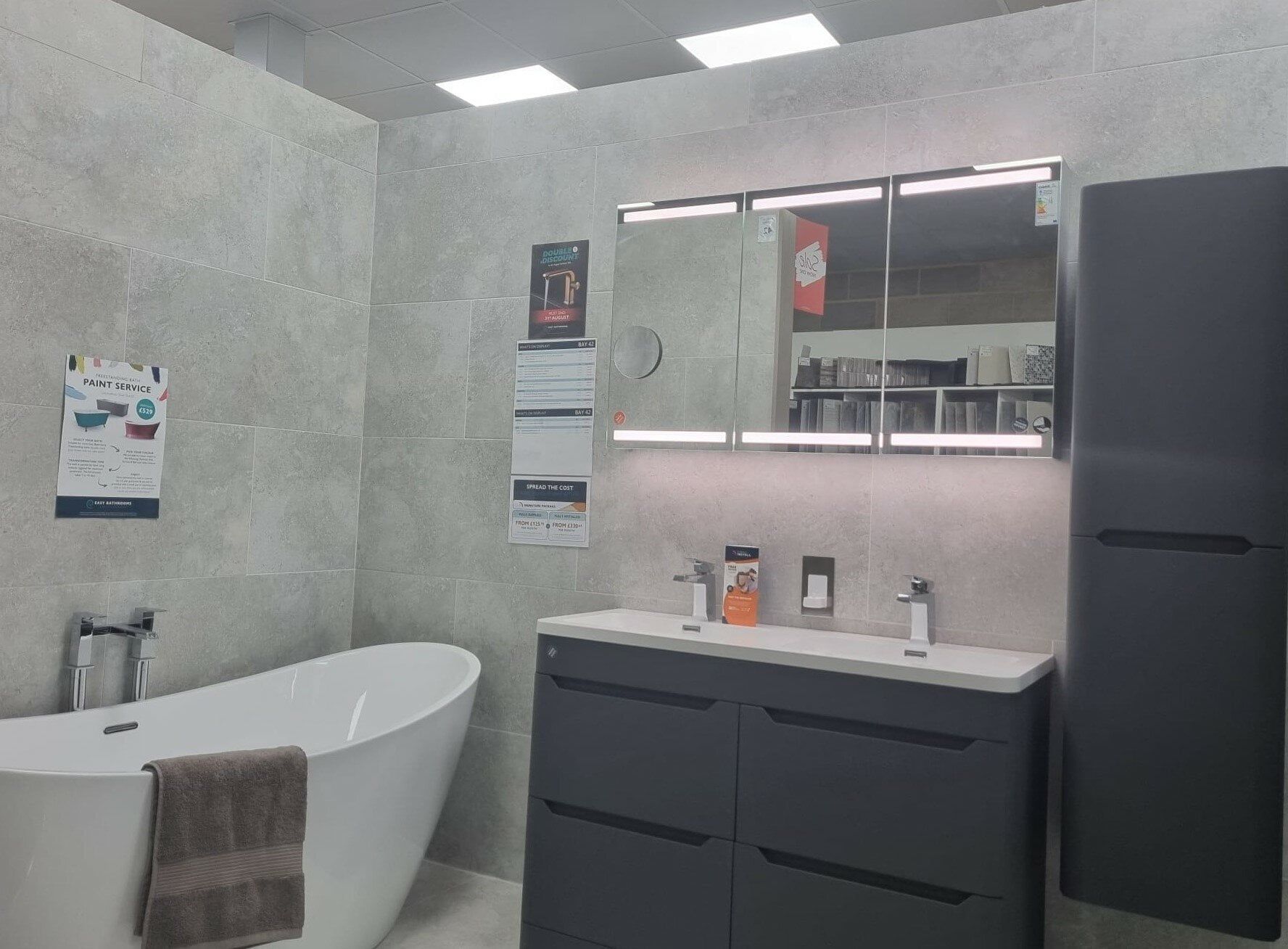 Modern Ellis bathroom furniture display at Easy Bathrooms Watford featuring dark vanity units, integrated handles, white basin and neutral wall tiles.