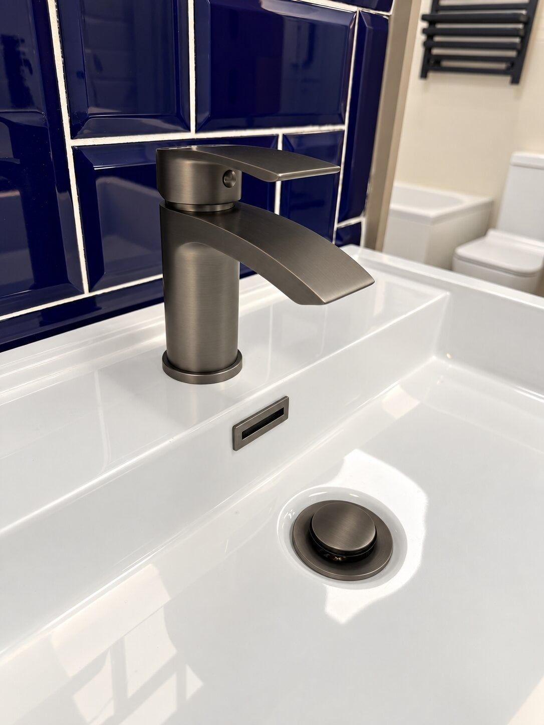 Gunmetal bathroom tap on display at Easy Bathrooms St Albans with a white basin and dark blue tiles.