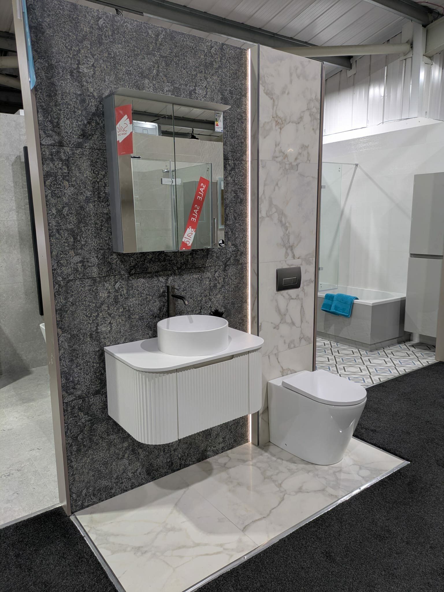 Contemporary bathroom display at Easy Bathrooms Bolton featuring grey marble-effect tiles, white furniture and illuminated mirror.