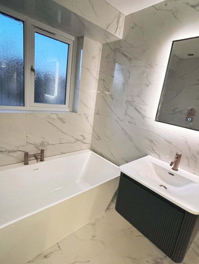 A contemporary bathroom featuring a Milo white freestanding acrylic bath and a charcoal Wish ribbed wall-hung vanity unit, accented by Moray satin bronze knurled brassware and Stockholm Odlina marble-effect gloss porcelain tiles.