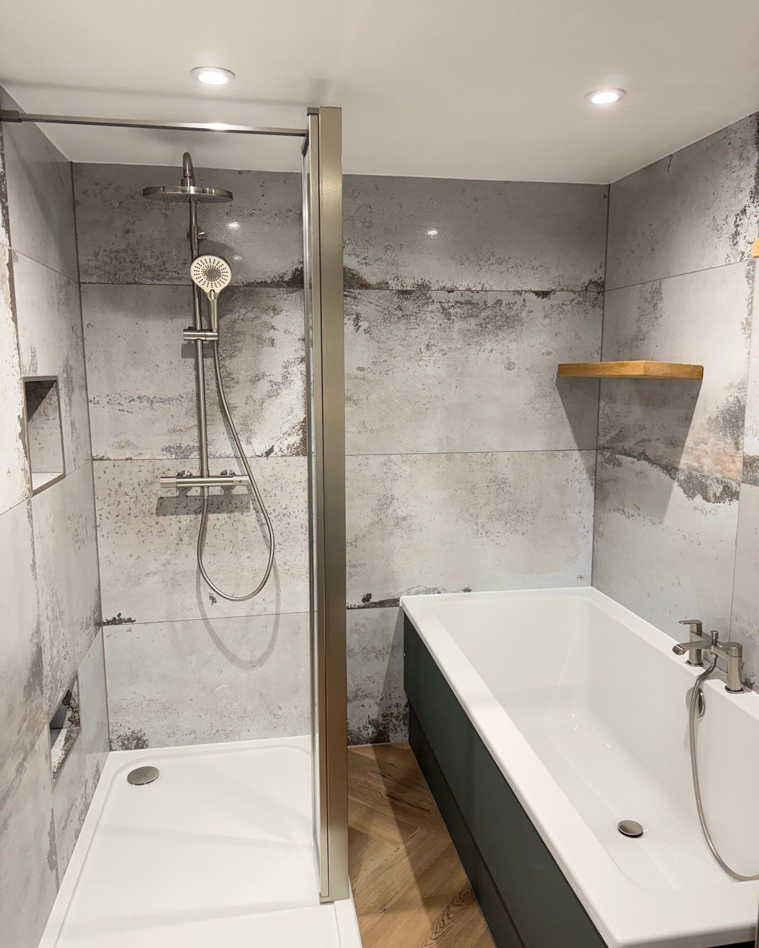 Finished bathroom featuring a bath with shower screen, overhead shower and marble-effect wall tiles.