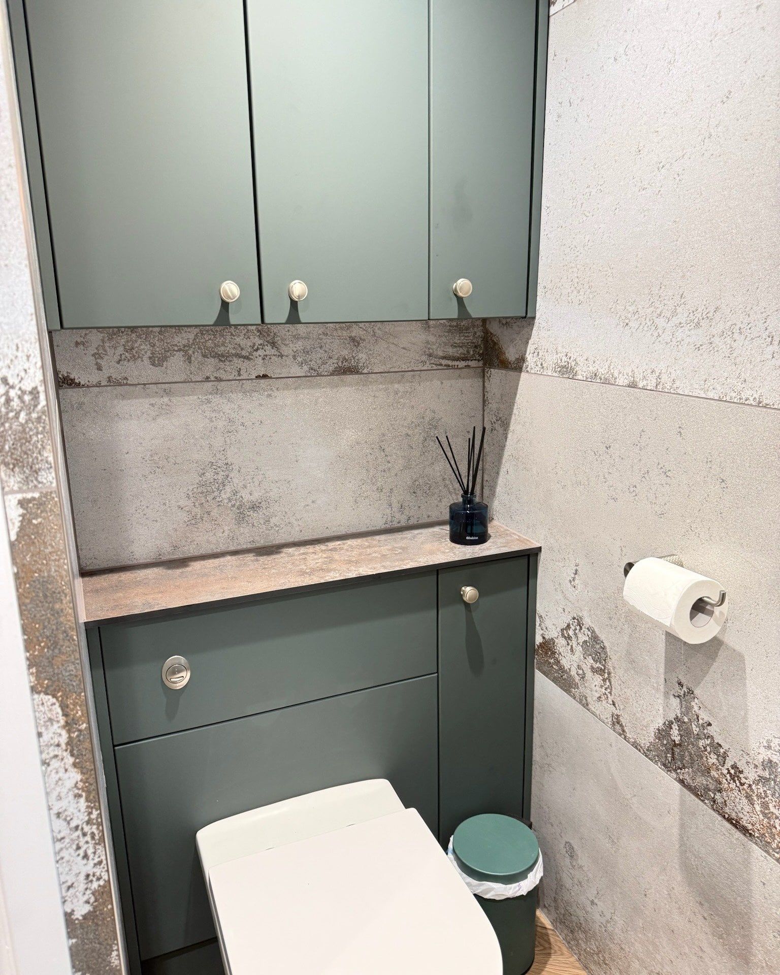 Finished bathroom with green fitted furniture, concealed cistern toilet and marble-effect wall tiles.