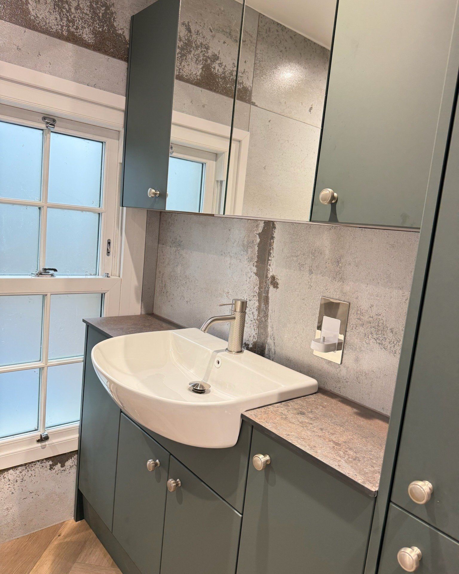 Finished bathroom with a grey vanity unit, illuminated mirror, basin and tiled splashback beside a window
