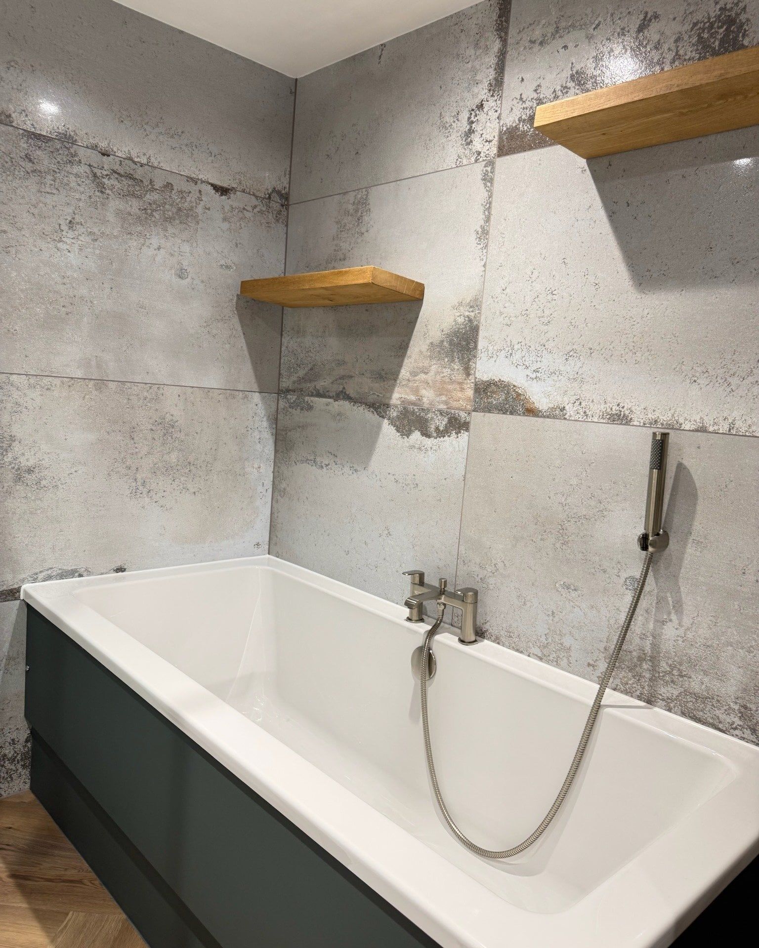 Finished bath and shower area with marble-effect tiles, chrome fittings and wooden display shelves.