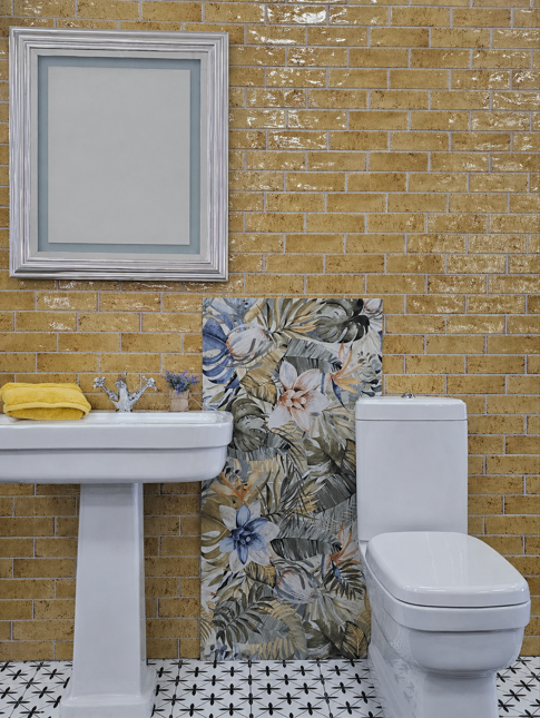 Bathroom display featuring mustard gloss metro tiles, a white pedestal basin and toilet, botanical feature tiles and patterned flooring.