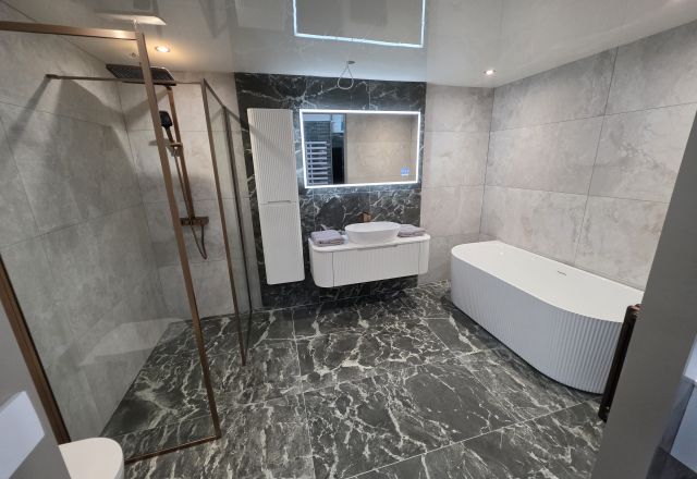 Bathroom display featuring black marble effect tiles, LED mirror and copper trim shower screen