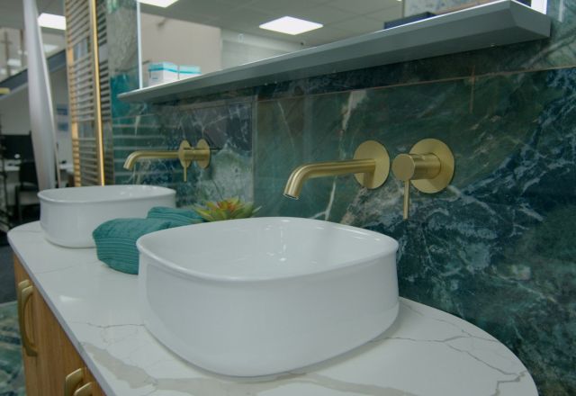 Showroom bathroom furniture display featuring modern counter top sinks, gold taps and emerald green marble tiles