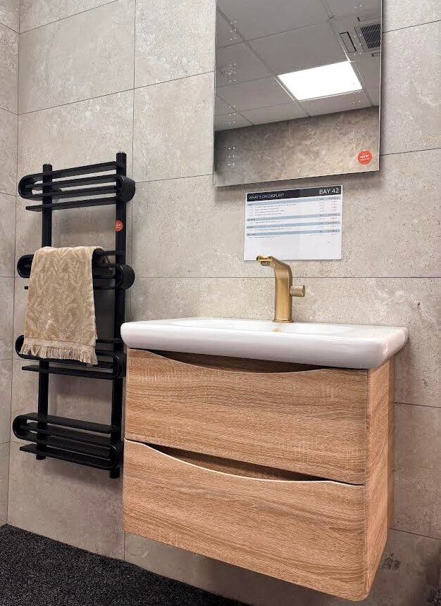 Bathroom showroom display featuring heated towel rail, wooden vanity unit and gold hardware