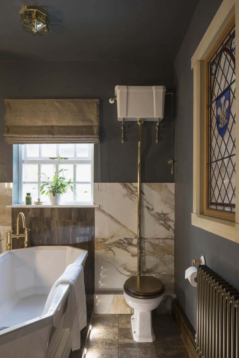 Burlington high level WC with gold pipe and oak seat next to a freestanding bath with Charlie Beige tiles.