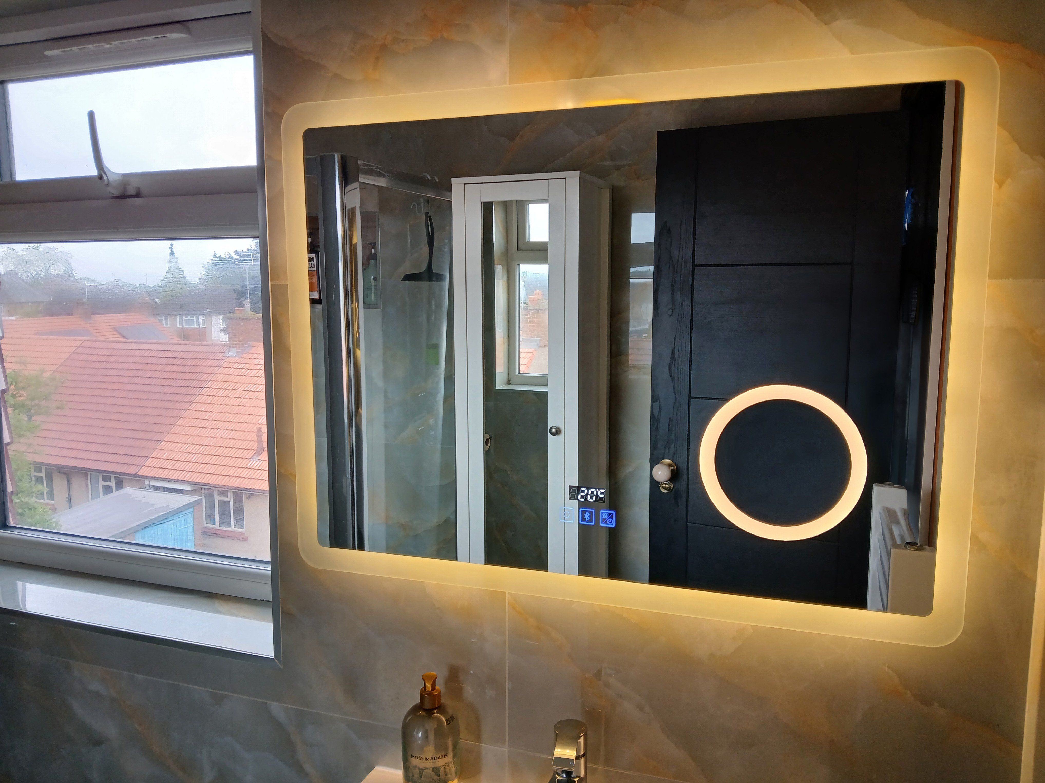 Illuminated rectangular bathroom mirror with integrated magnifying mirror and digital controls above marble-effect wall tiles