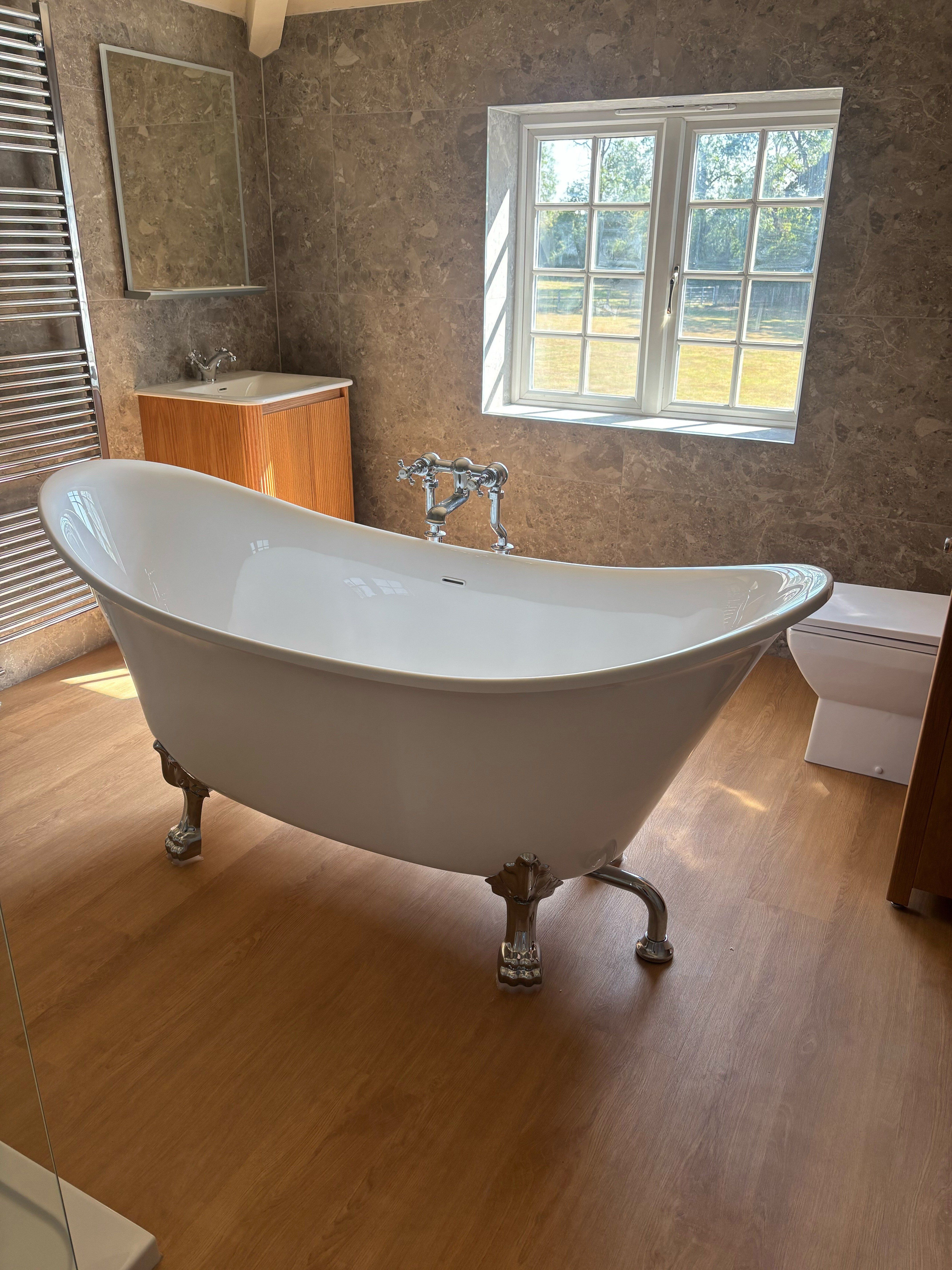Freestanding white bath with chrome feet, wood-effect flooring and neutral stone-effect tiles.