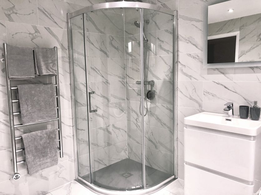 A modern quadrant glass shower enclosure with chrome trim, positioned next to a white gloss vanity unit and a polished chrome heated towel rail.