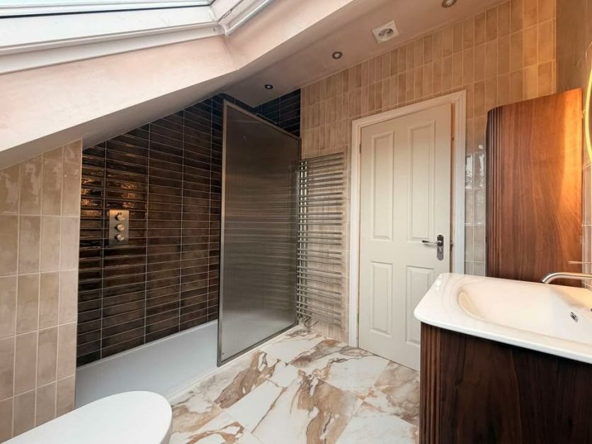 Elegant fluted glass shower and luxurious wood vanity on stunning marble tiles in a sleek loft conversion.