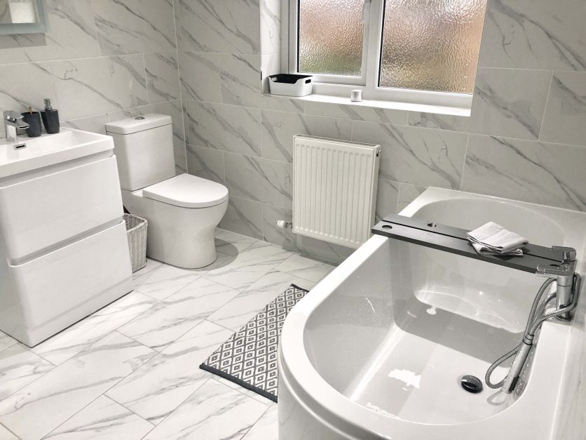 Modern bathroom featuring floor-to-ceiling white marble effect tiles, a contemporary d-shaped bath, and a sleek white gloss vanity unit with chrome taps.