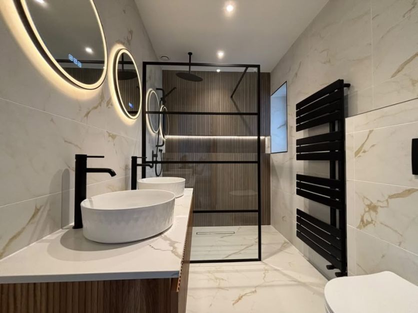 A modern luxury wetroom featuring a matt black Amien framed shower screen and Zena rainfall head, set against Madera Roble slatted wood tiles and Dune Marble matt porcelain flooring with a matching dual countertop basin vanity.