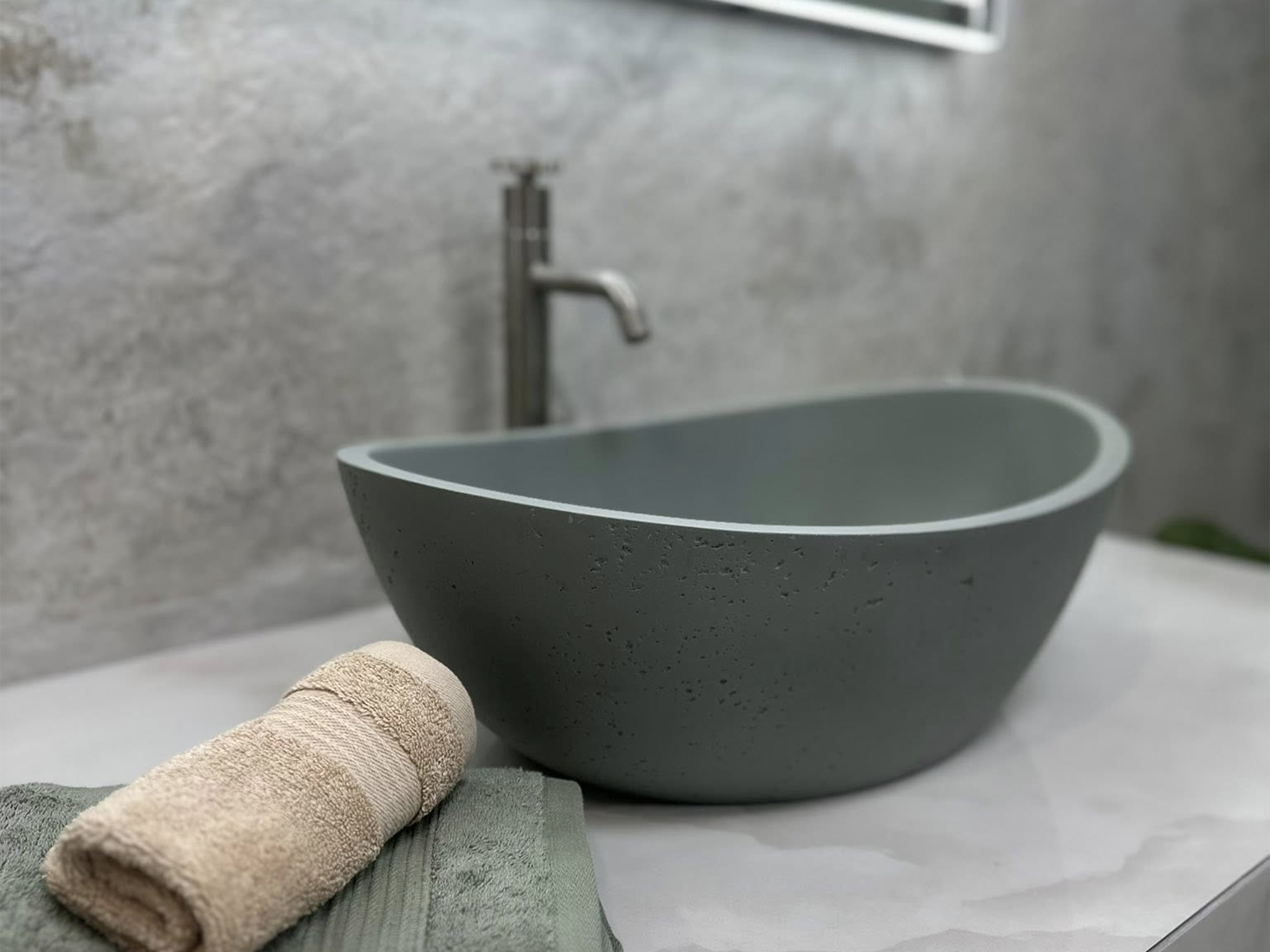 Close-up of a grey stone basin with a black basin tap, folded towels and marble-effect wall tiles