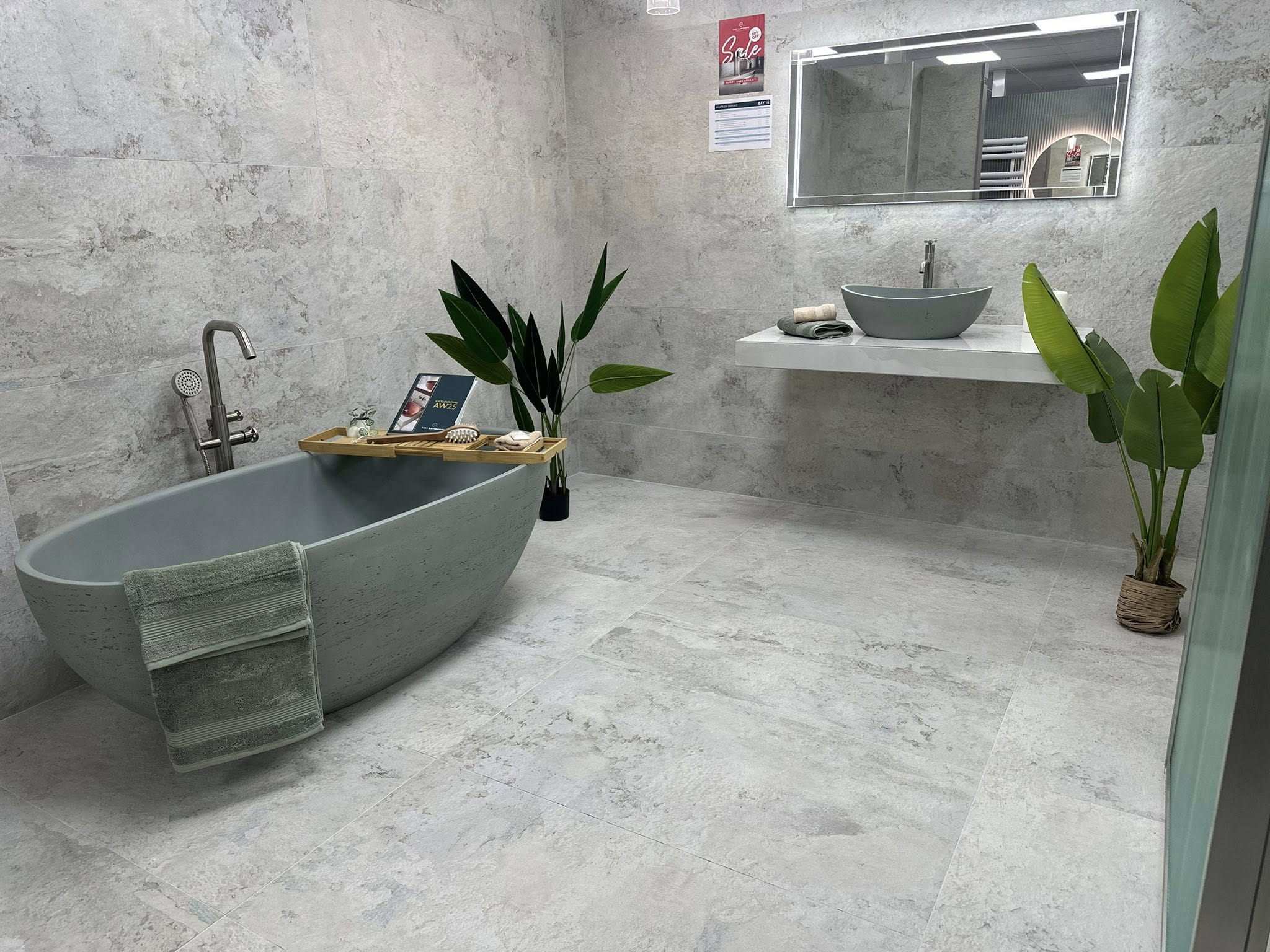 Finished bathroom featuring a freestanding grey bath, black wall-mounted tap, large-format grey tiles and green plants