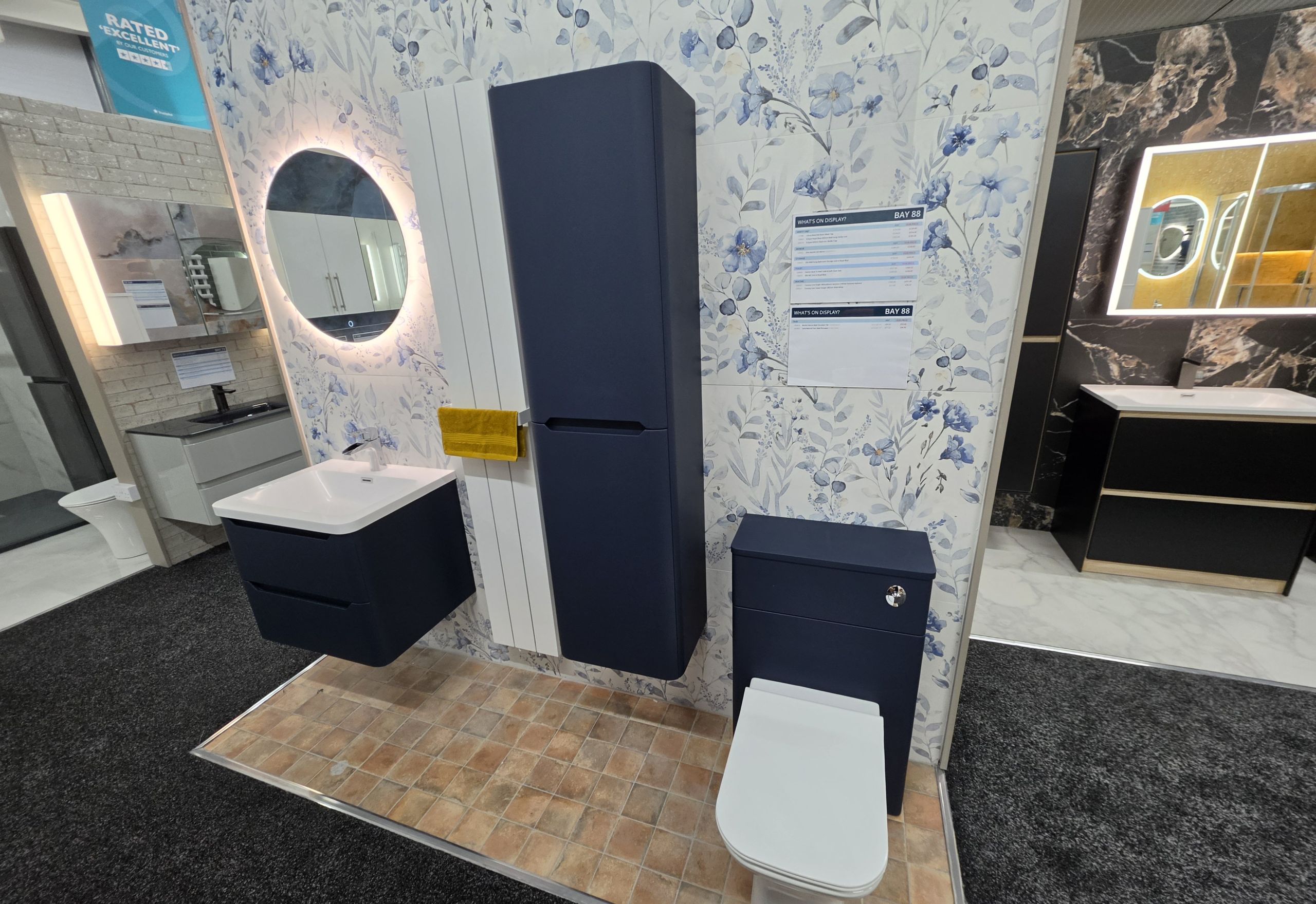 Bathroom display featuring blue floral tiles, wall hung cabinets and basin and navy backed toilet